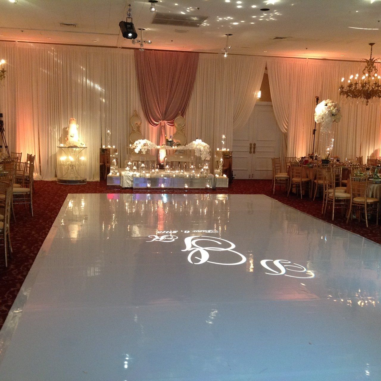A large room with a white dance floor and tables and chairs.