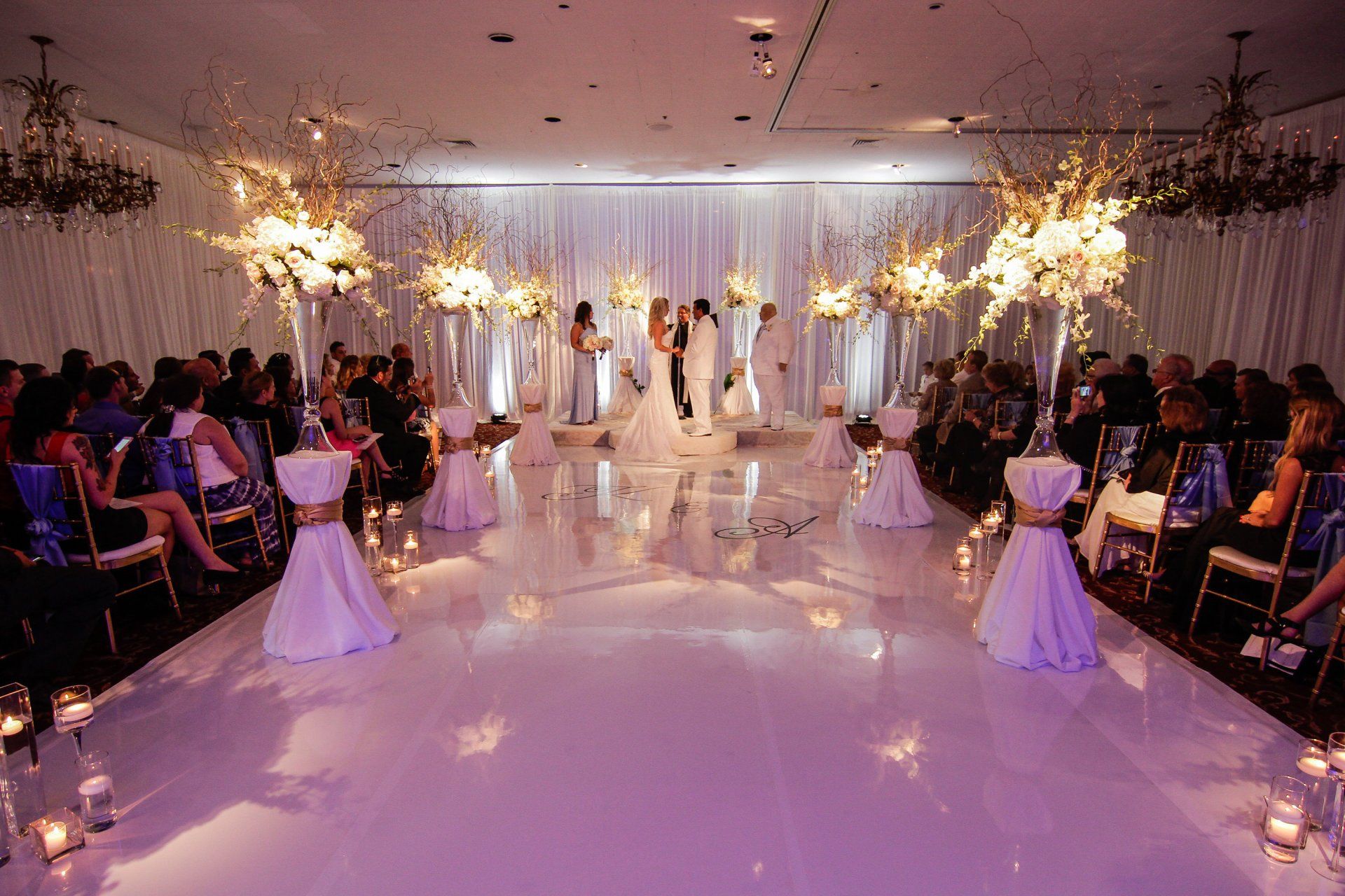 A wedding ceremony is taking place in a large room with a white floor.