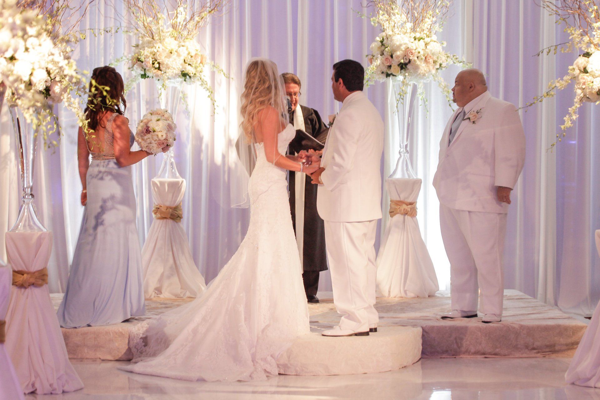 A bride and groom are getting married in front of a purple curtain.