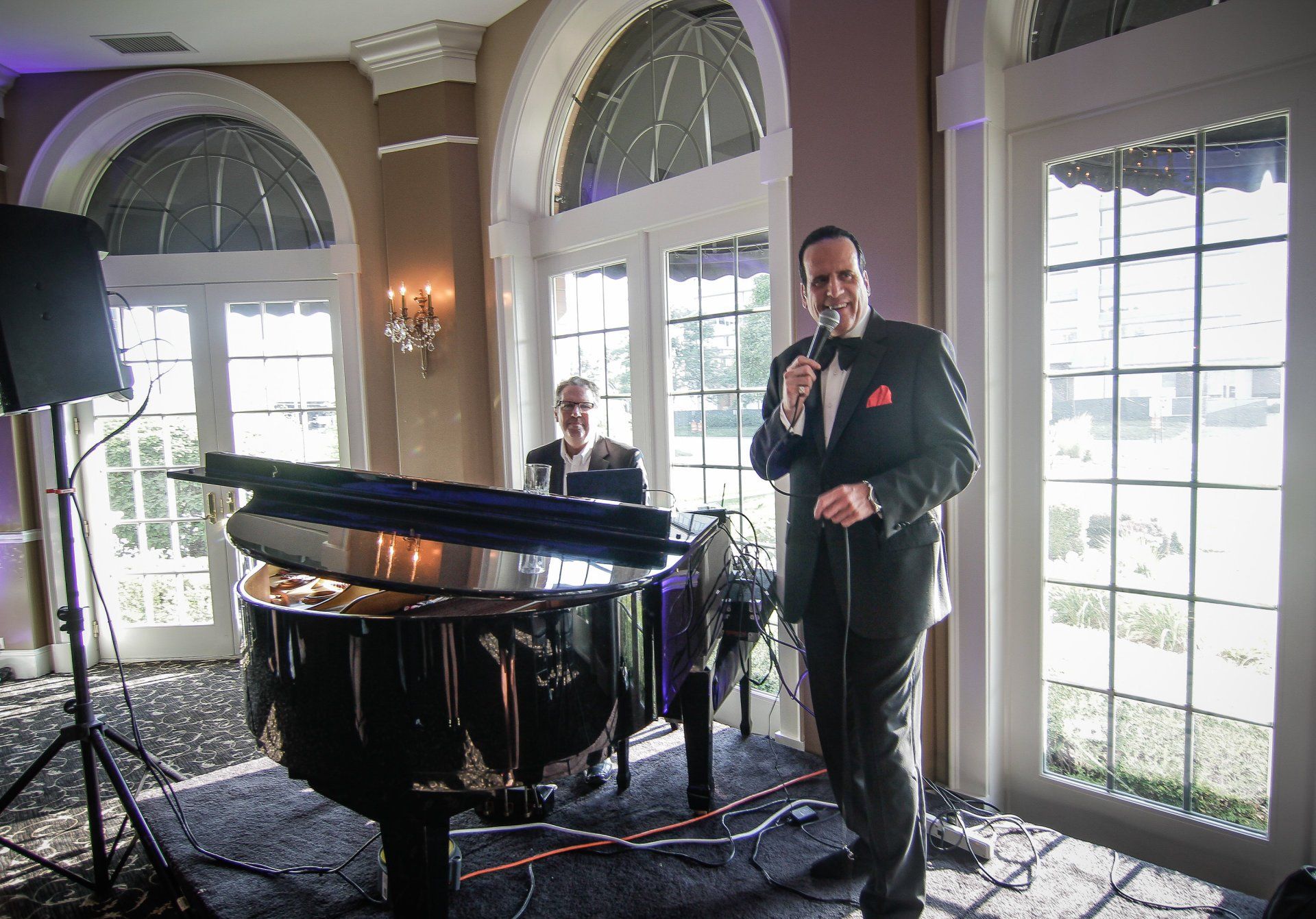 A man in a tuxedo is singing into a microphone in front of a piano.