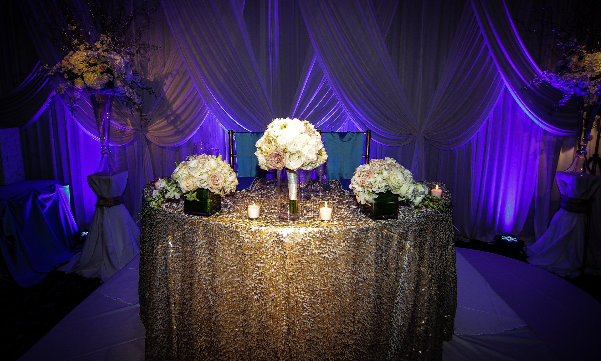 A table with flowers and candles on it in a room with purple lights.