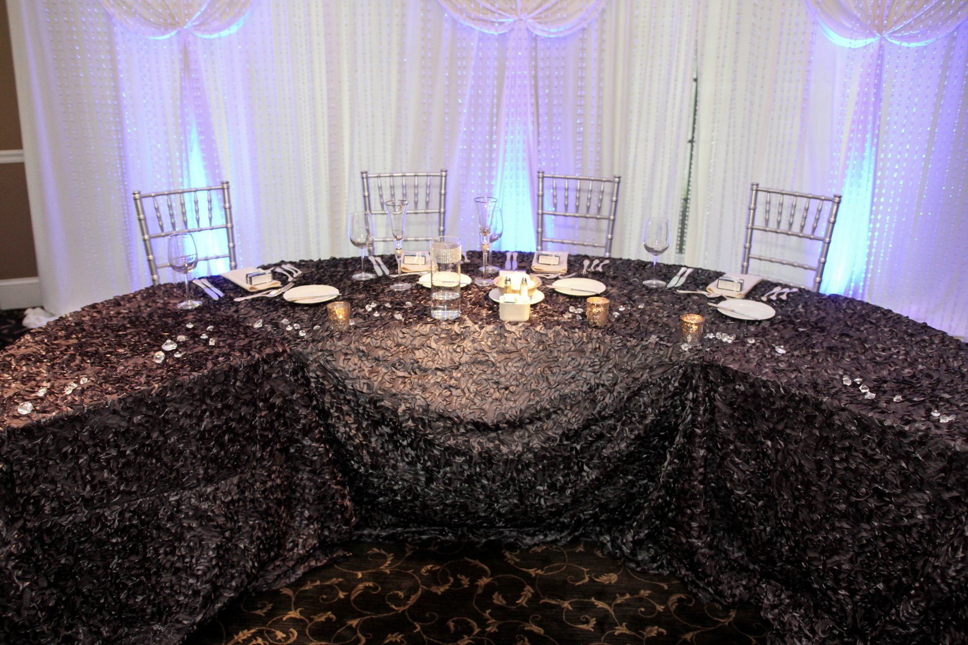 A round table with a black tablecloth and candles on it.