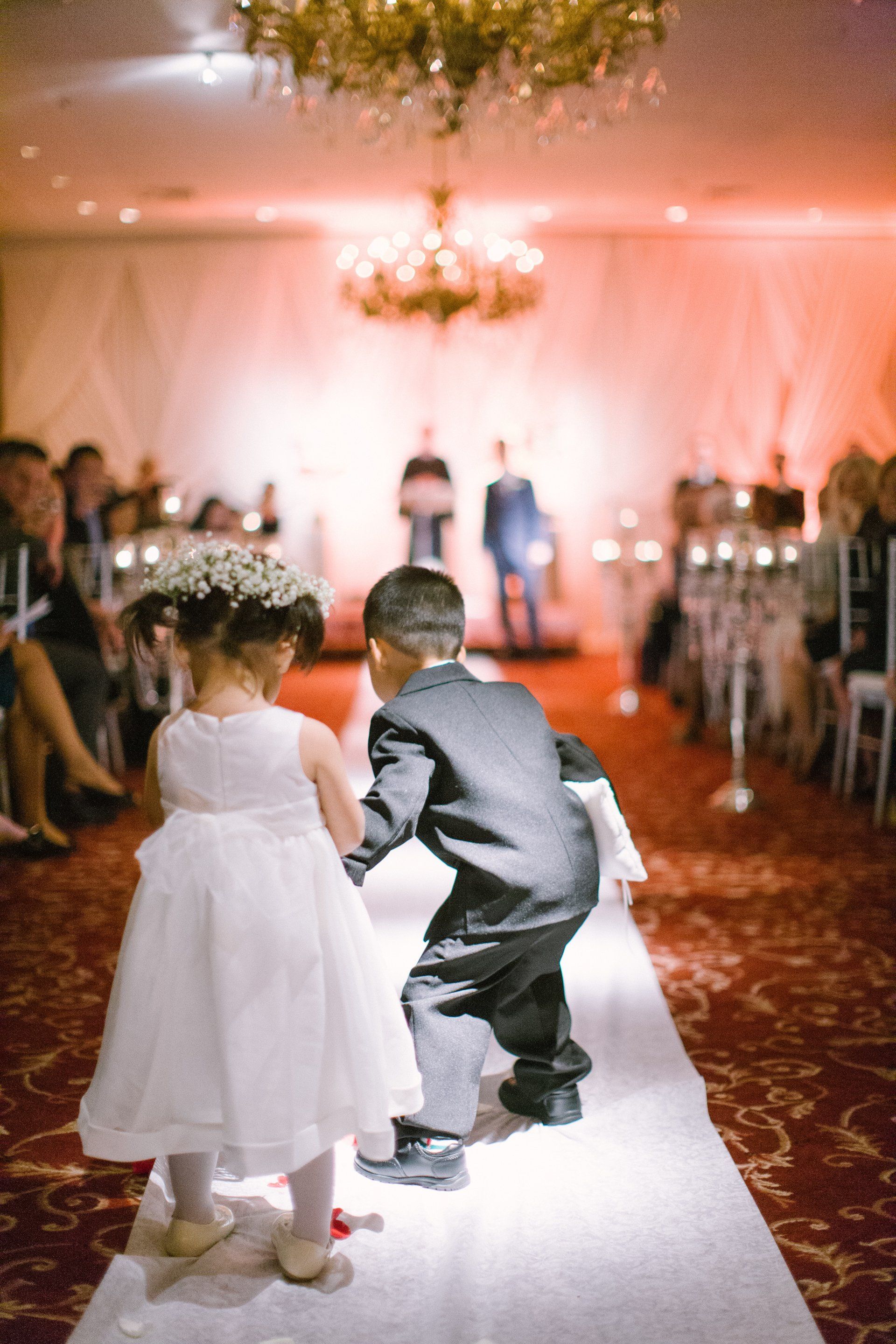 A flower girl and a ring bearer are walking down the aisle at a wedding.