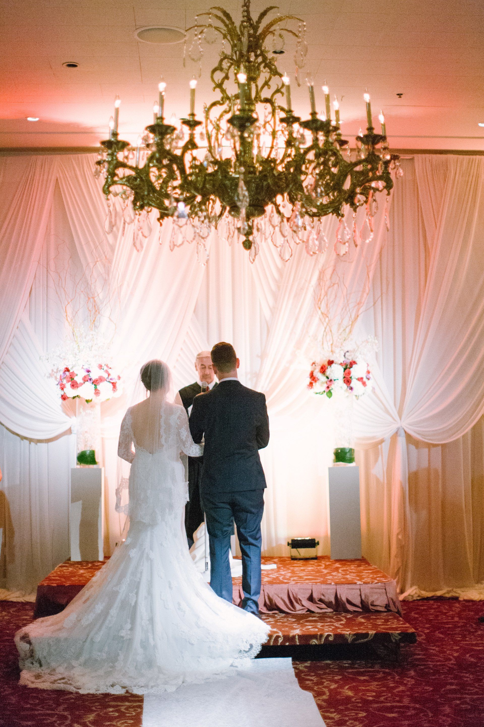 A bride and groom are standing in front of a chandelier during their wedding ceremony.