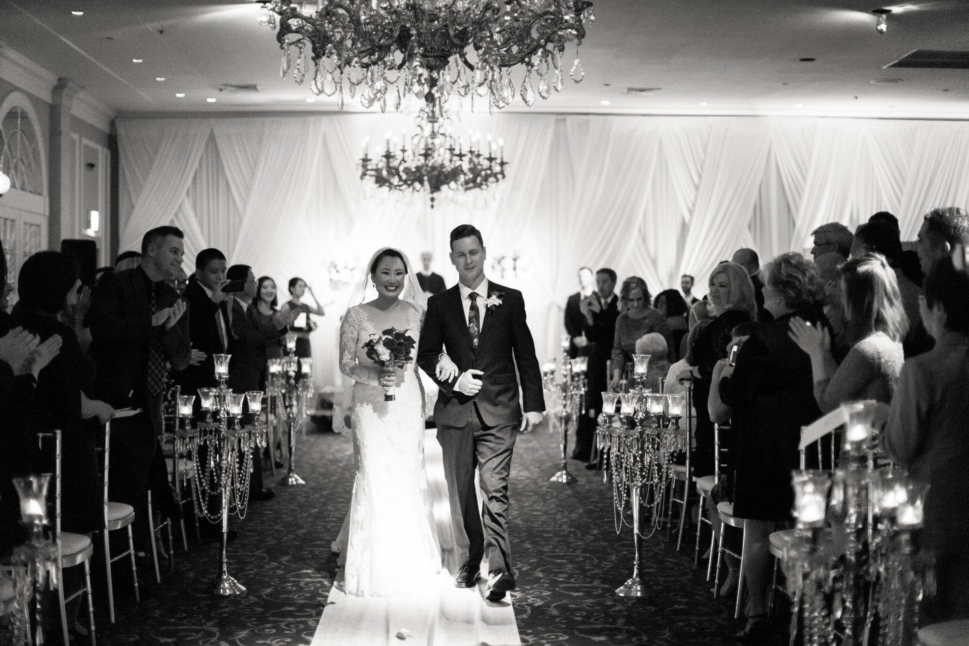 A black and white photo of a bride and groom walking down the aisle at their wedding.