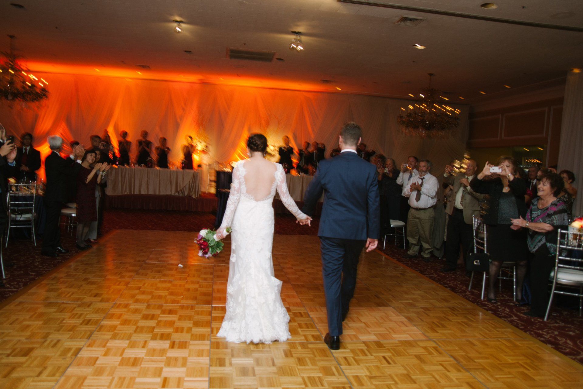 A bride and groom are walking down the dance floor at their wedding reception.