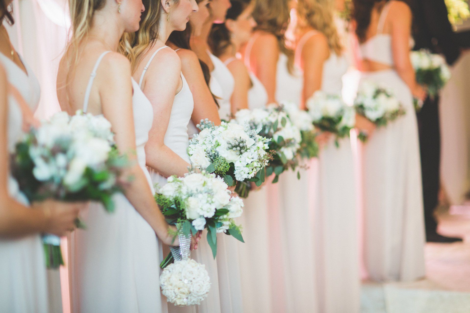A bride and her bridesmaids are standing in a line holding bouquets of white flowers.