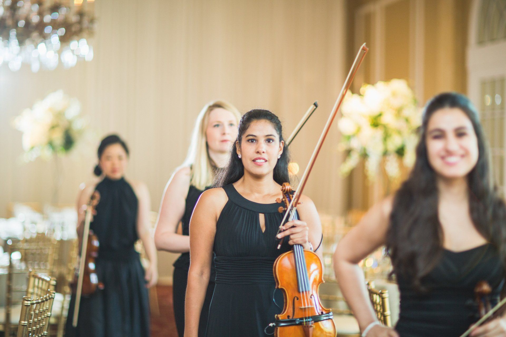 A woman is holding a violin in front of a group of women playing violins.