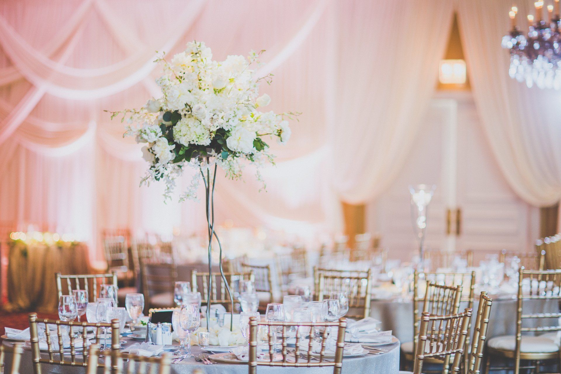 A large vase filled with white flowers is on a table at a wedding reception.