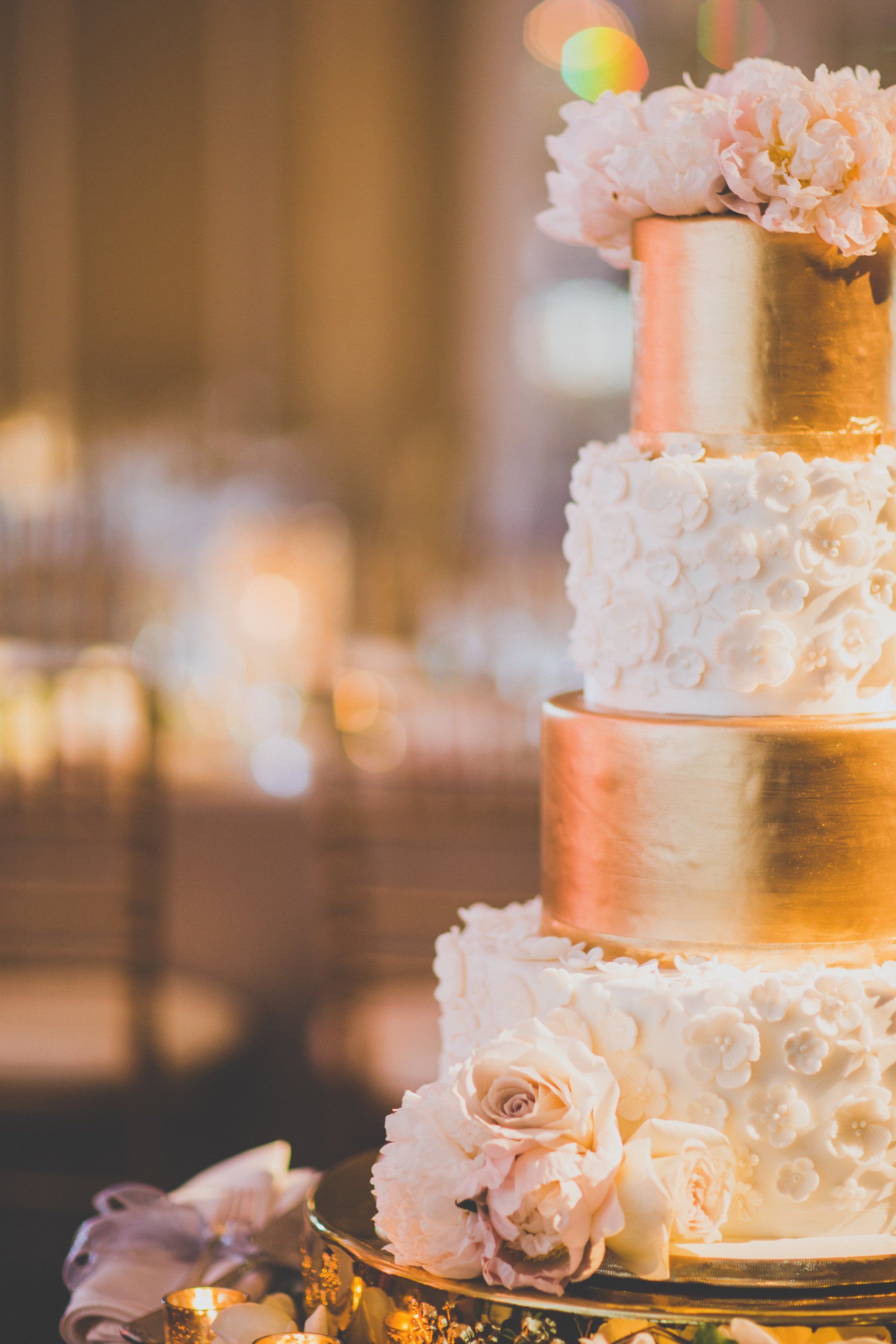 A white and gold wedding cake with flowers on top is on a table.