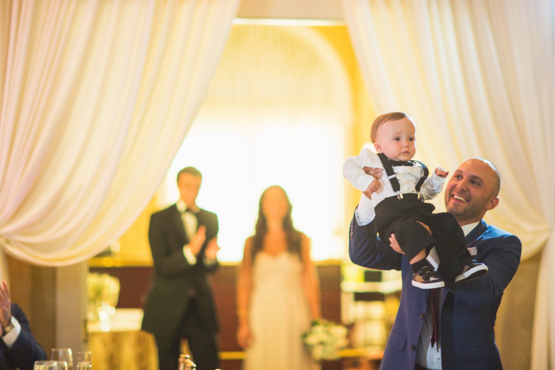 A man is holding a baby in his arms at a wedding reception.