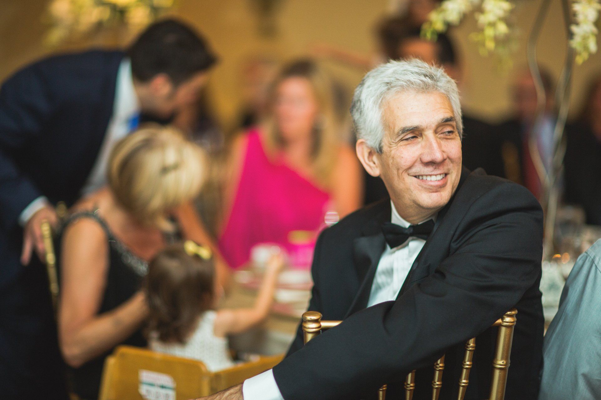 A man in a tuxedo is sitting in a chair at a wedding reception.