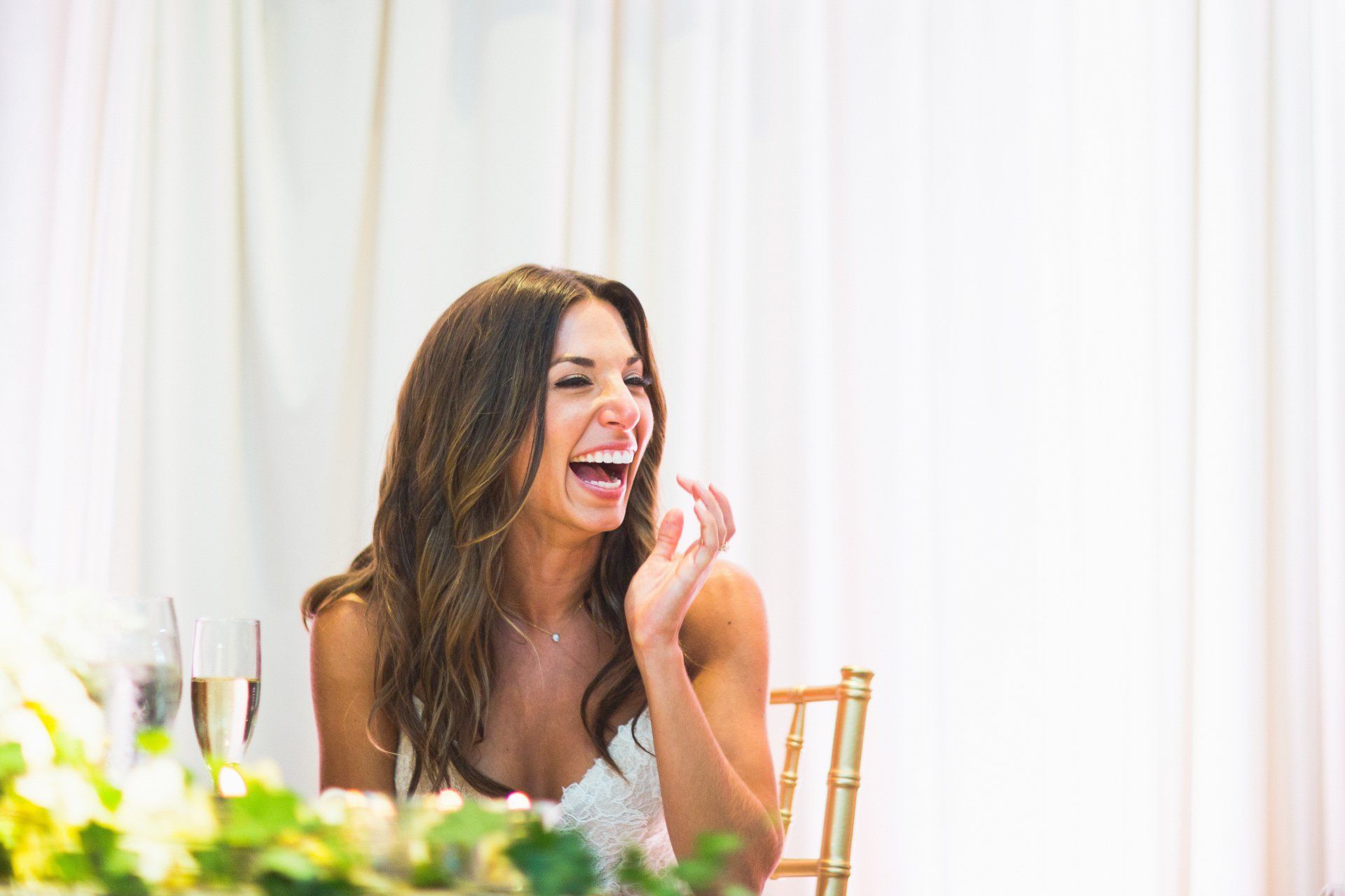 A woman is laughing while sitting at a table at a wedding reception.