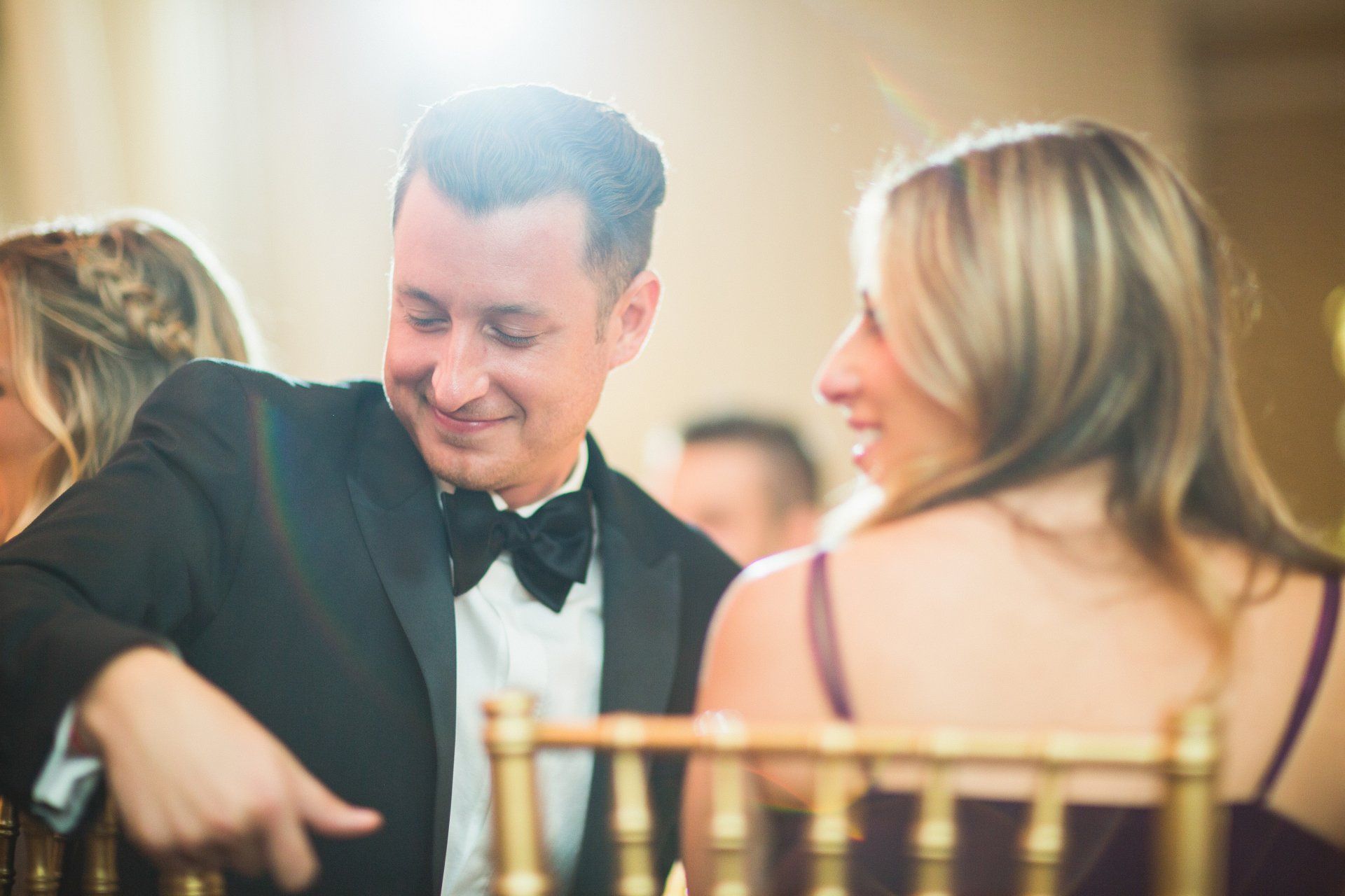 A man in a tuxedo is pointing at a woman while sitting in a chair.