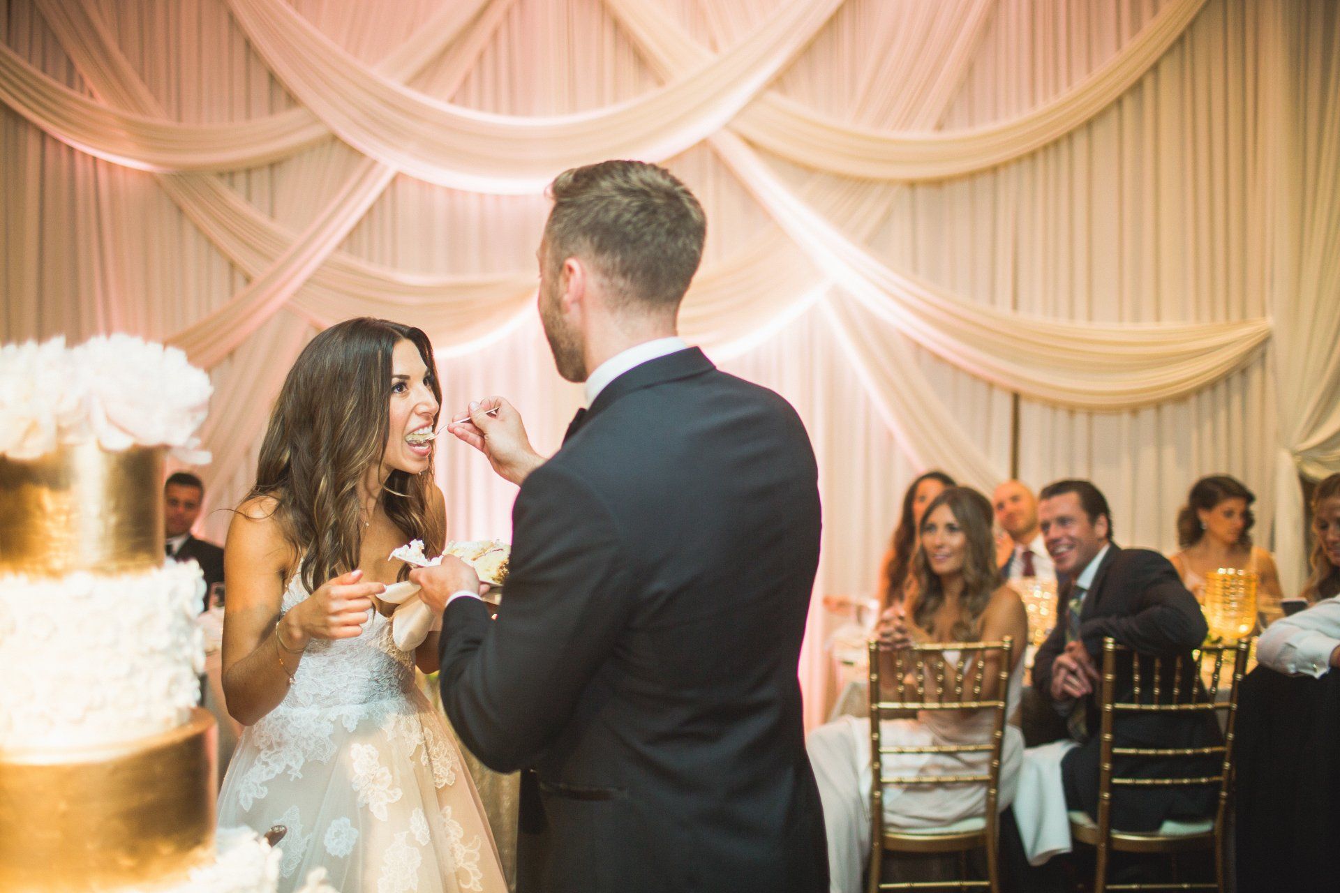 A bride and groom are cutting their wedding cake in front of their wedding guests.