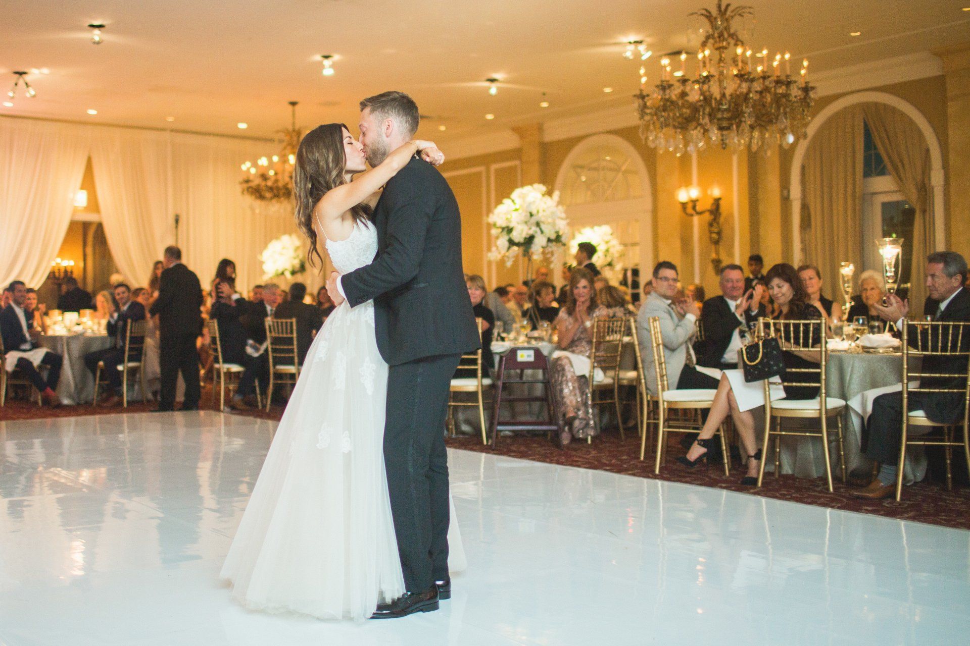 A bride and groom are kissing during their first dance at their wedding reception.