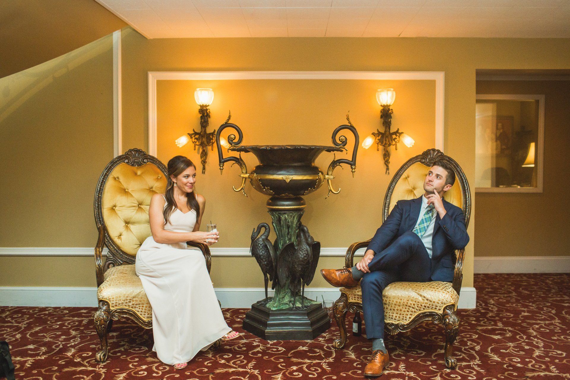 A bride and groom are sitting in chairs in front of a vase.