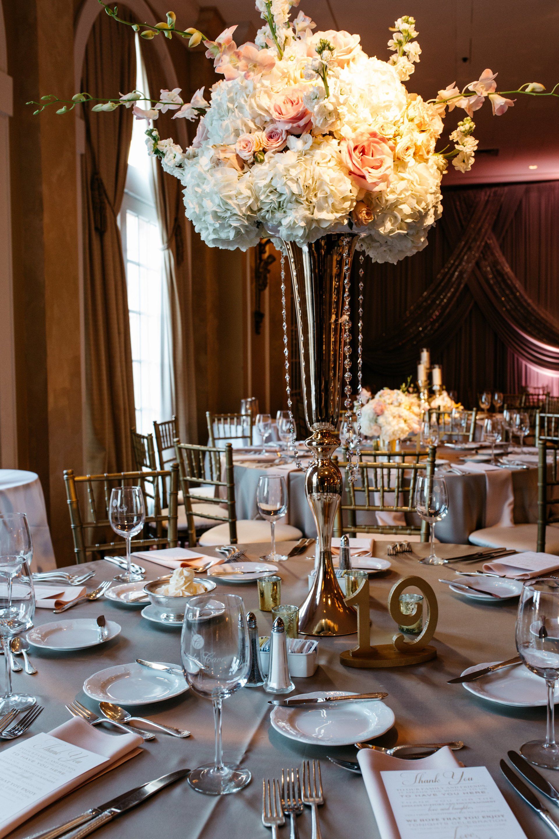 A table set for a wedding reception with a large vase of flowers on it.