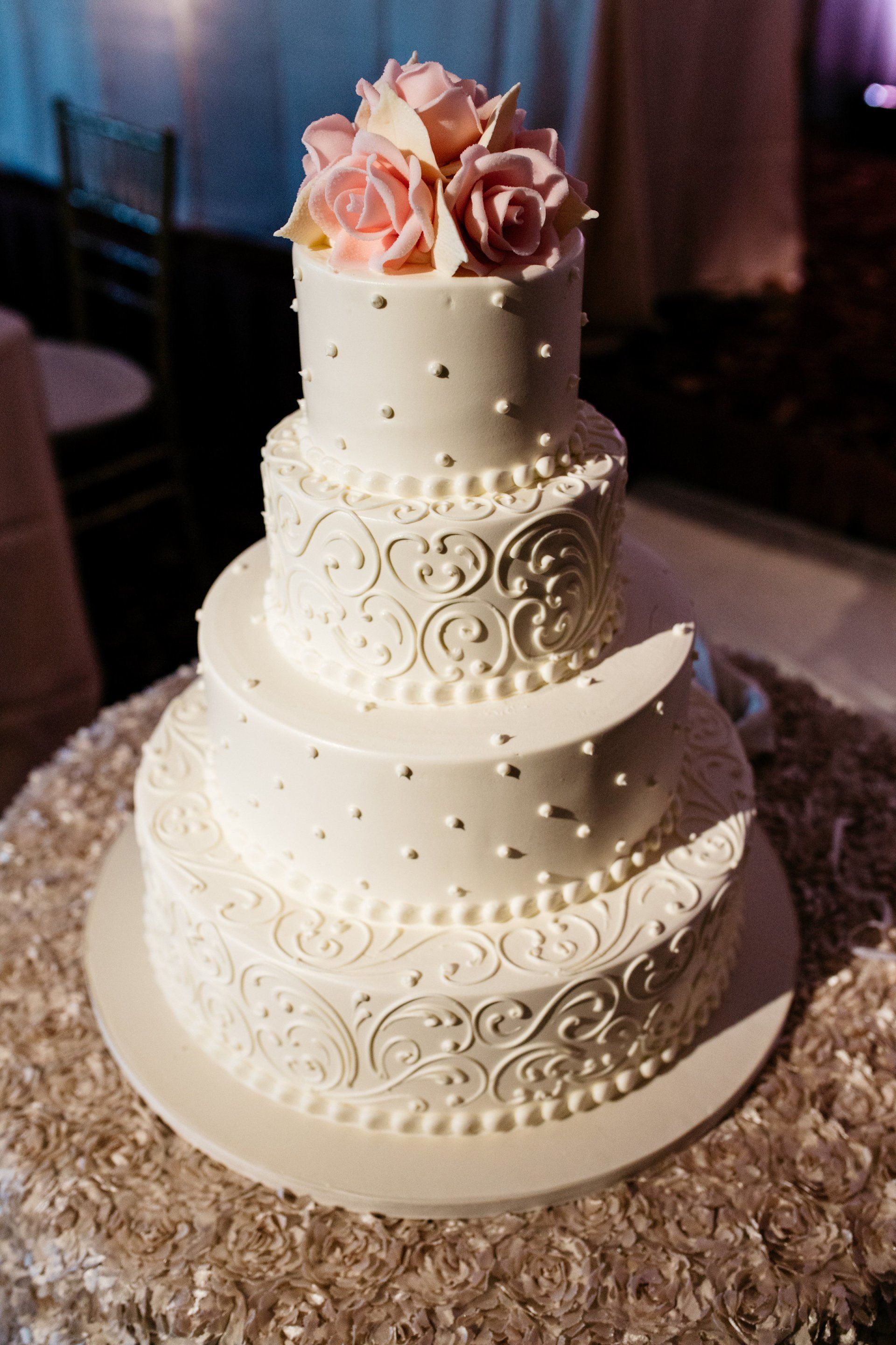 A white wedding cake with pink roses and pearls on top is sitting on a table.