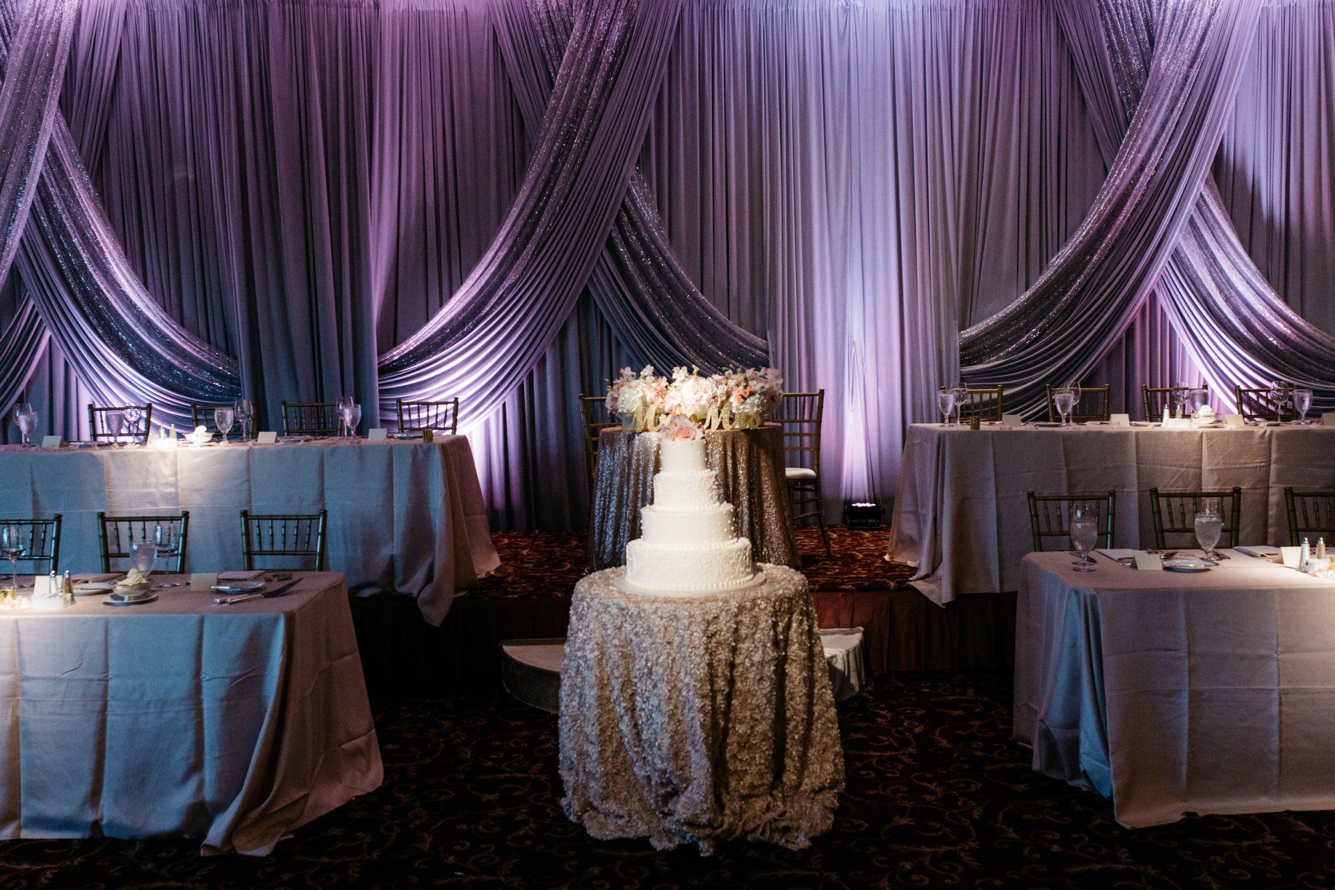 A wedding cake is sitting on a table in front of a purple curtain.
