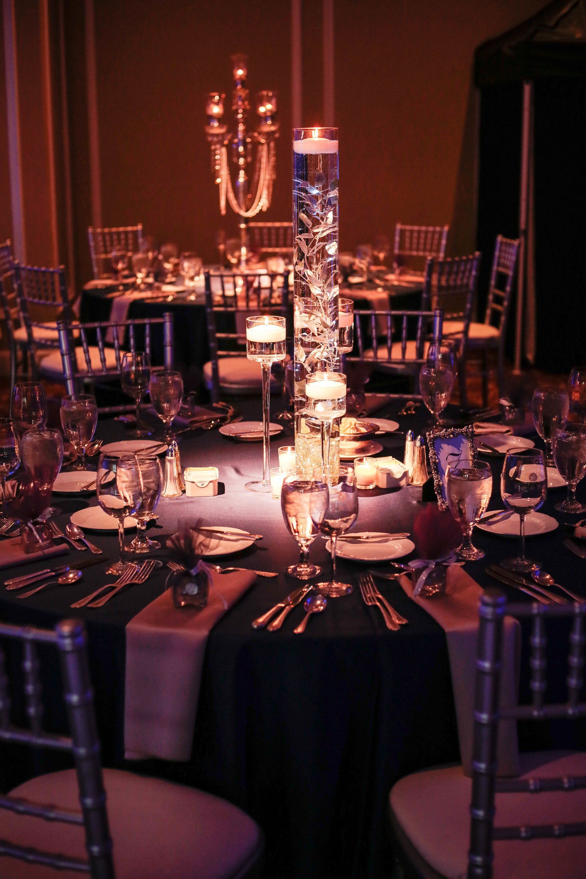 A table set for a wedding reception with a tall vase filled with candles