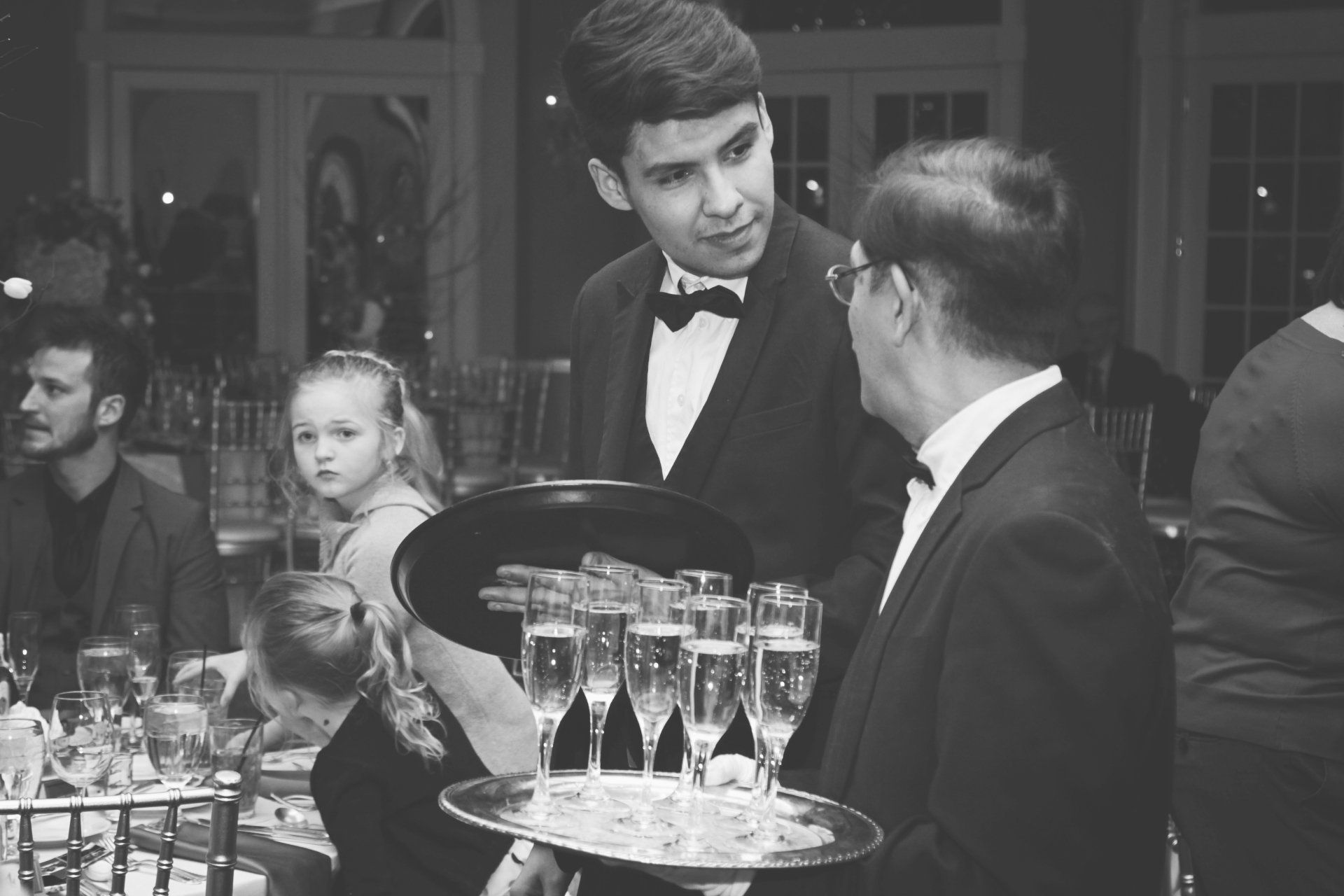 A man in a tuxedo is holding a tray of champagne glasses.