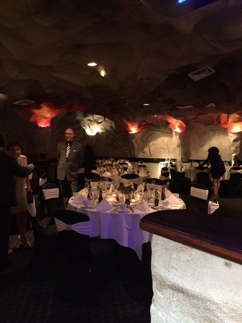 A man in a suit stands in a dark room with tables set for a party