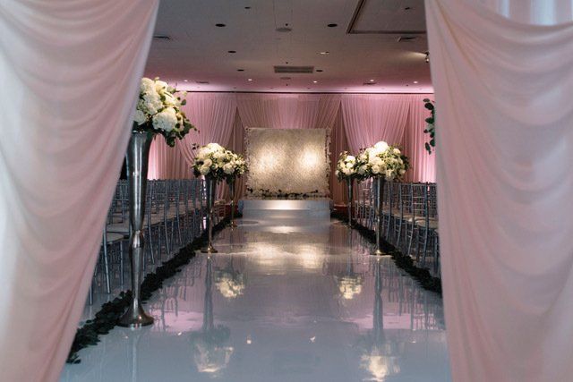 A wedding ceremony is taking place in a large room with a white aisle.