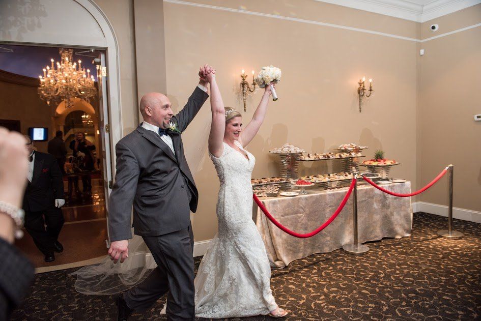 A bride and groom are walking into a room with their hands in the air.