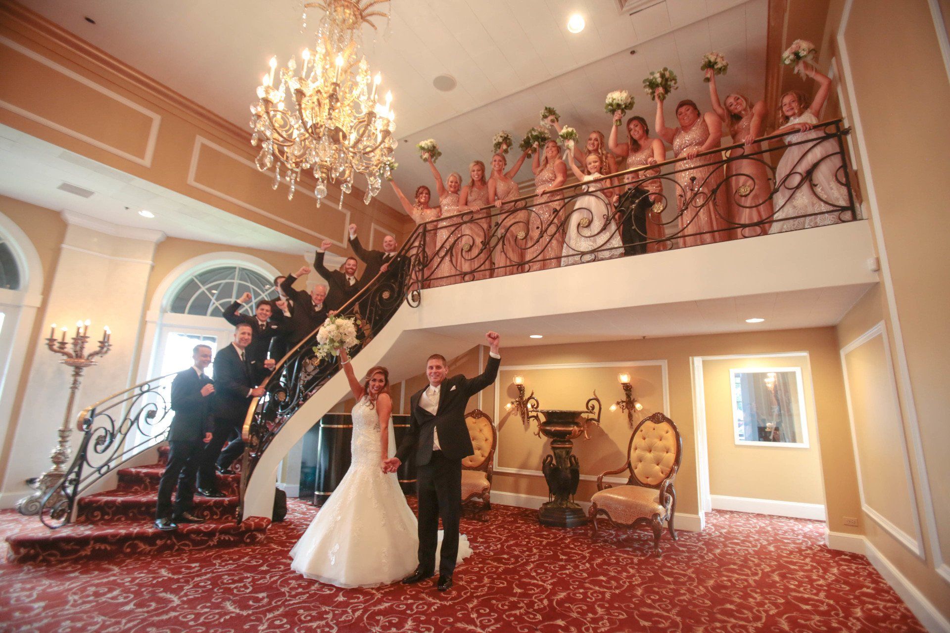 A bride and groom are standing on a staircase with their wedding party.