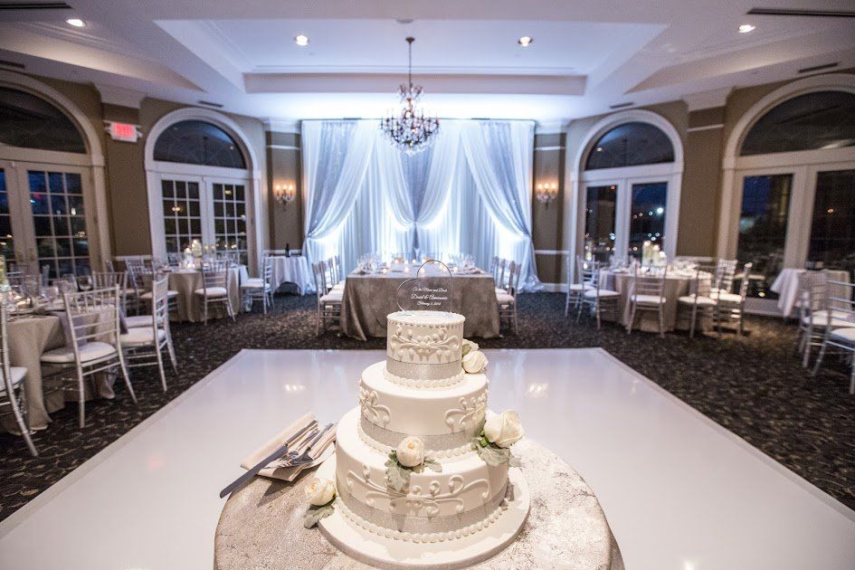A wedding cake is sitting on top of a white dance floor in a large room.
