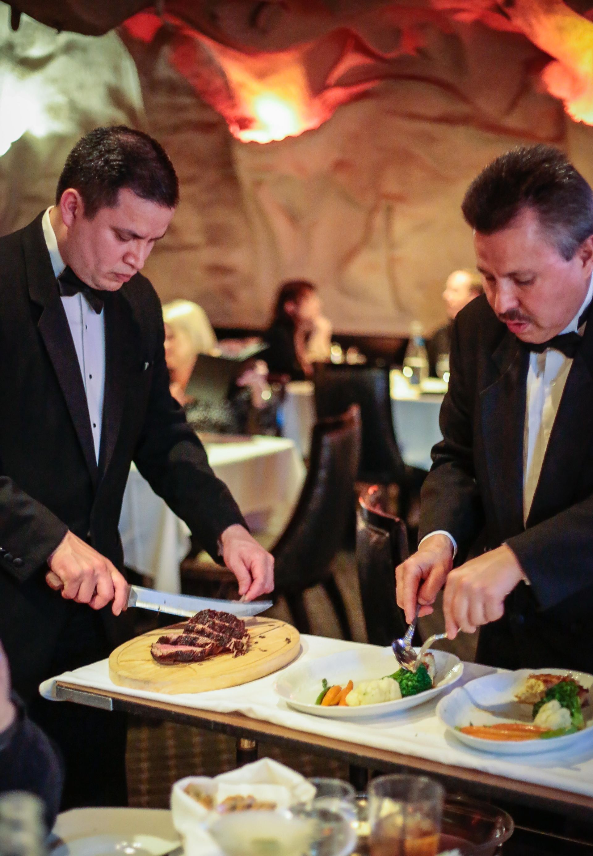 Two men in tuxedos are serving food in a restaurant