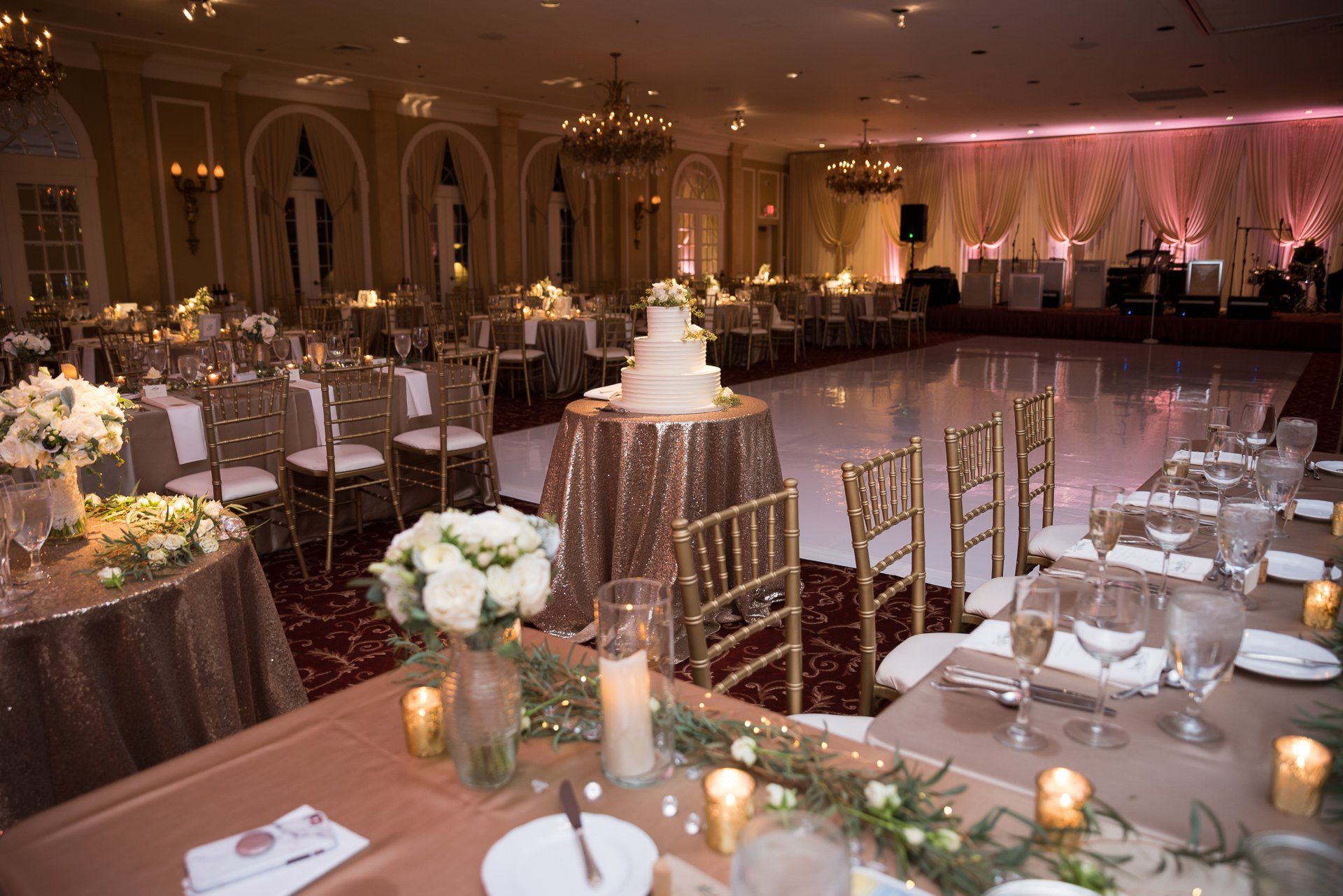 A large room with tables and chairs set up for a wedding reception with a cake on top of a table.