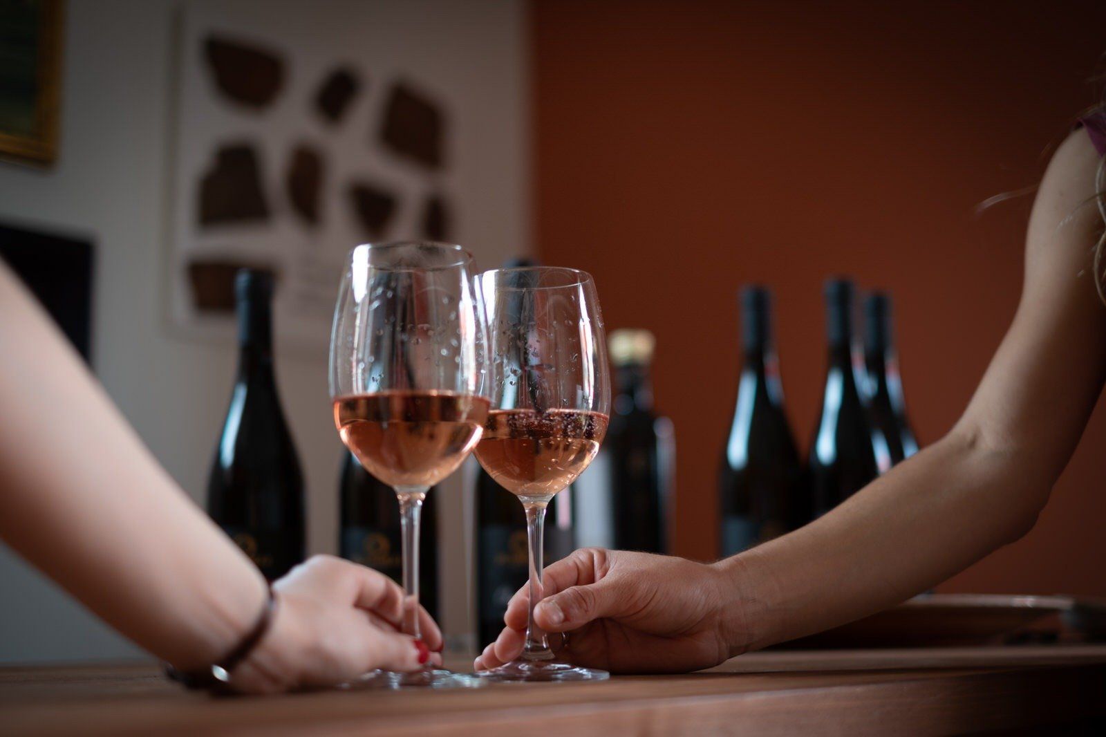 Braccia di due donne che reggono due calici di vino