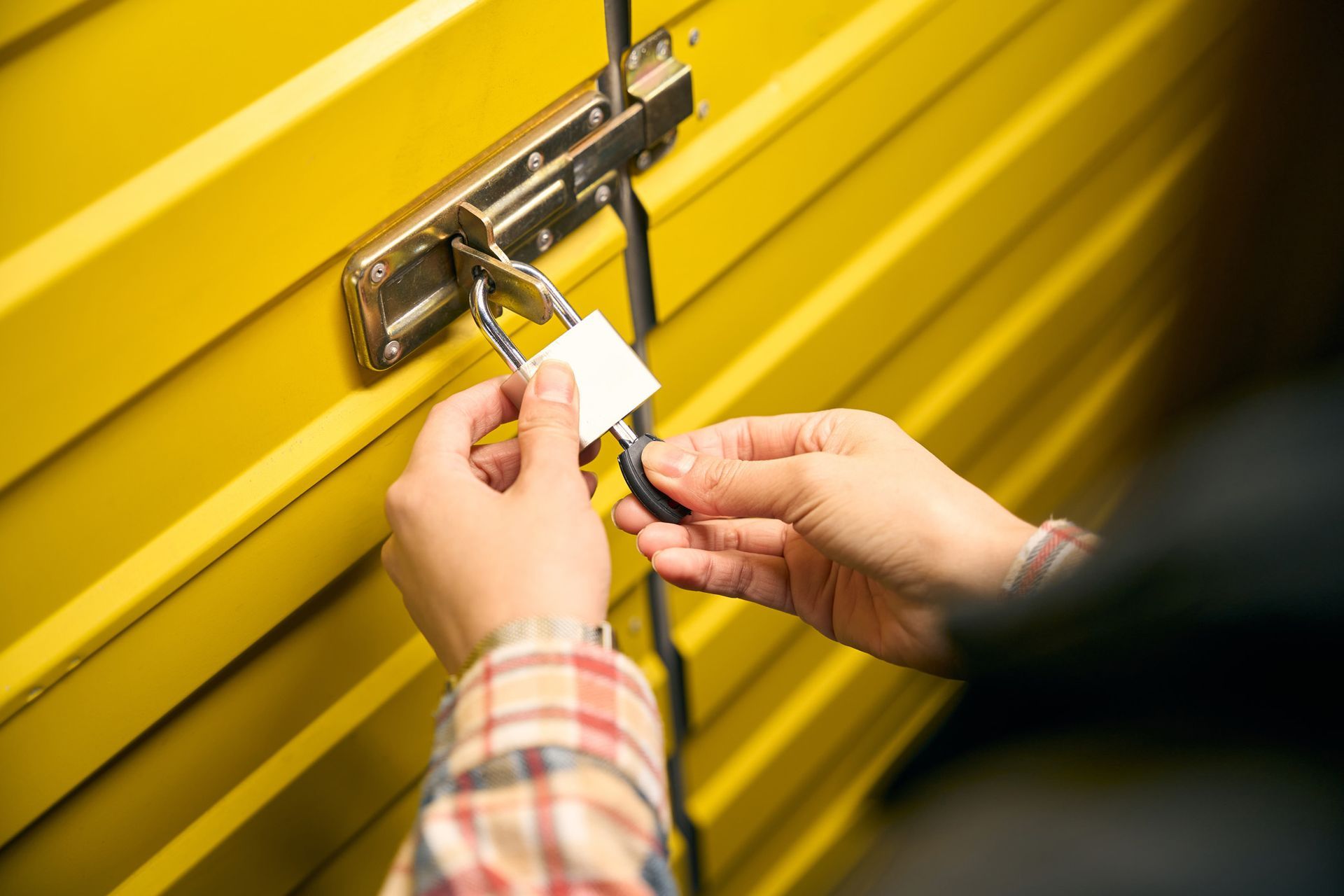 A person is locking a yellow garage door with a padlock.