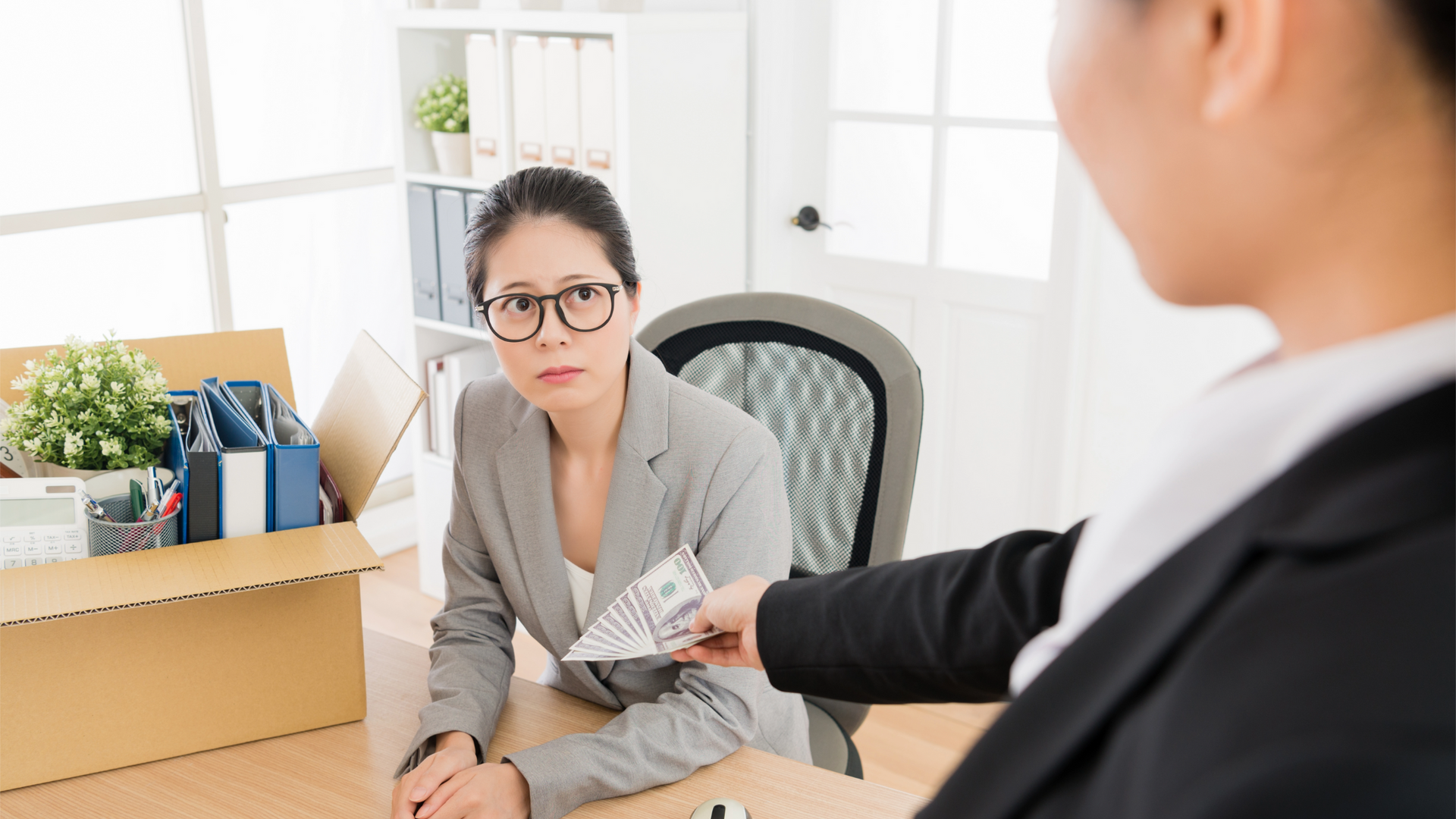 A woman is sitting at a desk while a man gives her money.