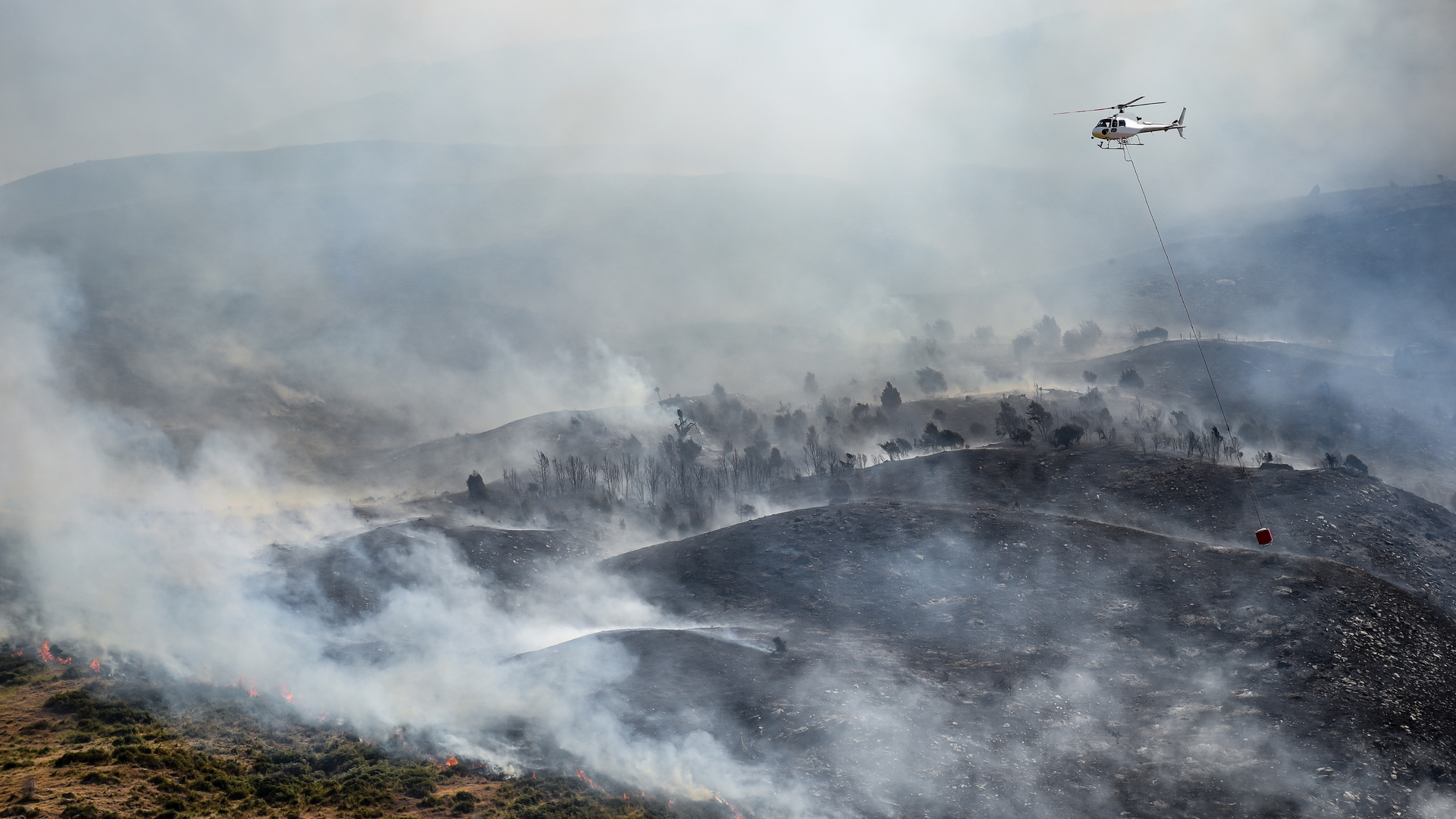 A helicopter is dropping water on a fire in the mountains.