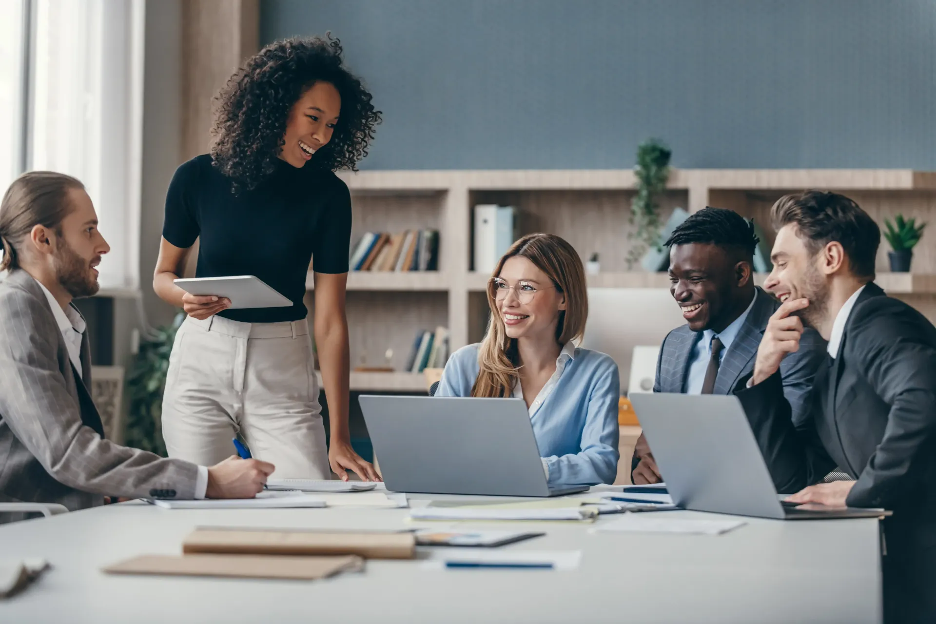 A group of business people are sitting around a table with laptops.