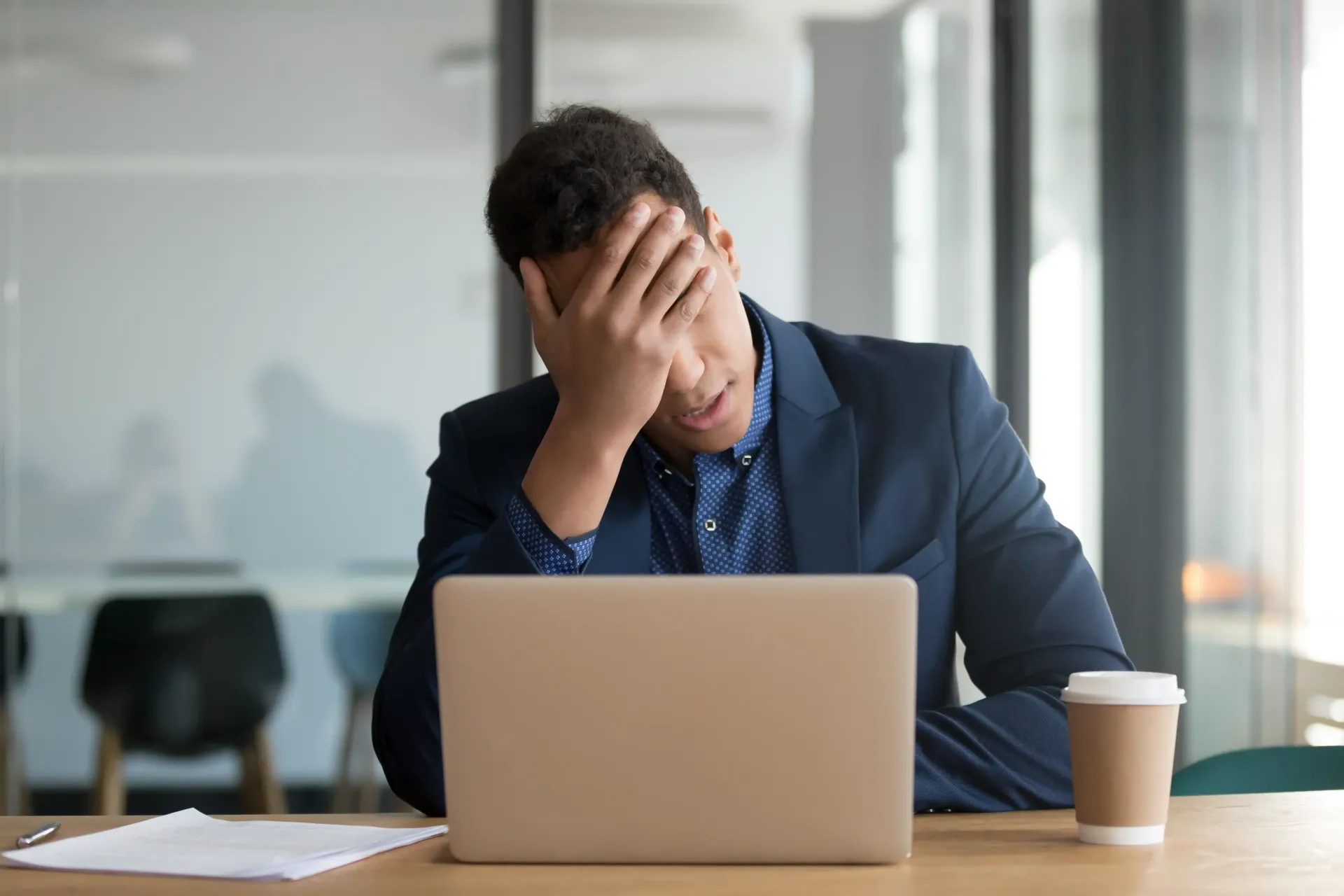 A man is sitting at a desk with his head in his hands in front of a laptop computer.