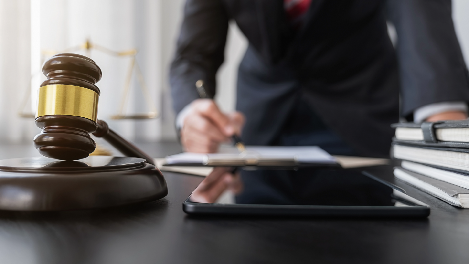 A lawyer is sitting at a desk with a gavel and a tablet, ready to file a lawsuit