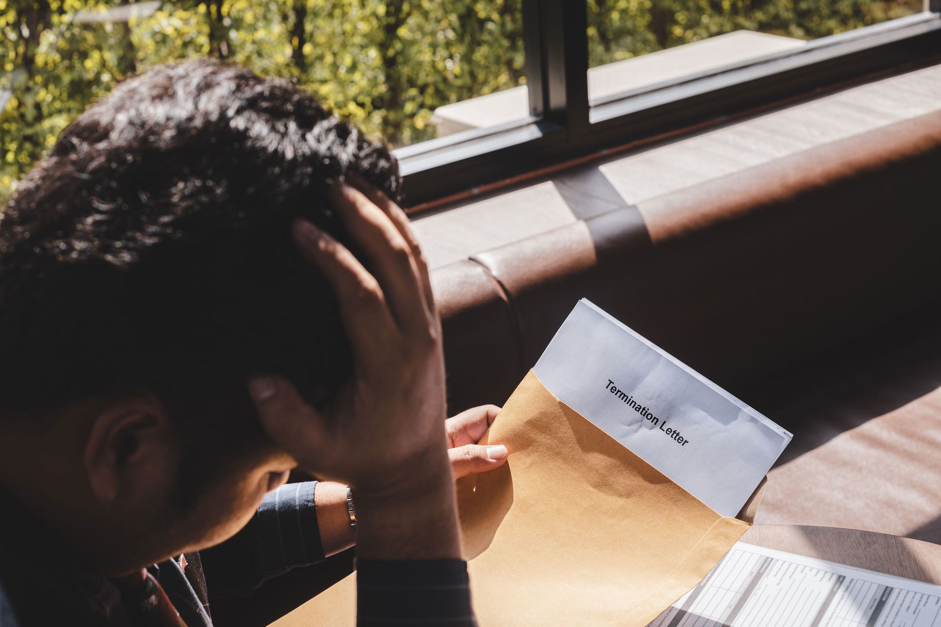 Angry looking man points at another man with his head in his hands at an office desk. 