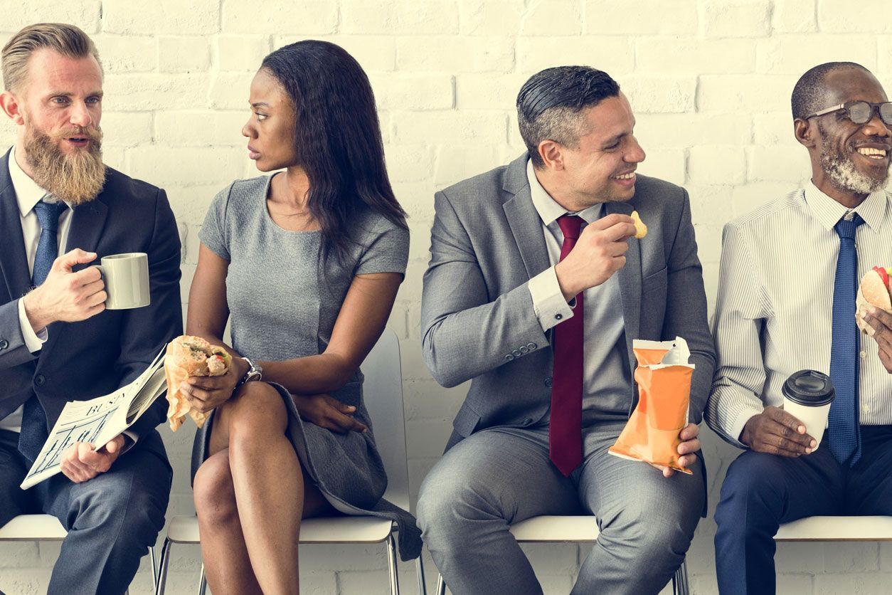 Angry looking man points at another man with his head in his hands at an office desk. 
