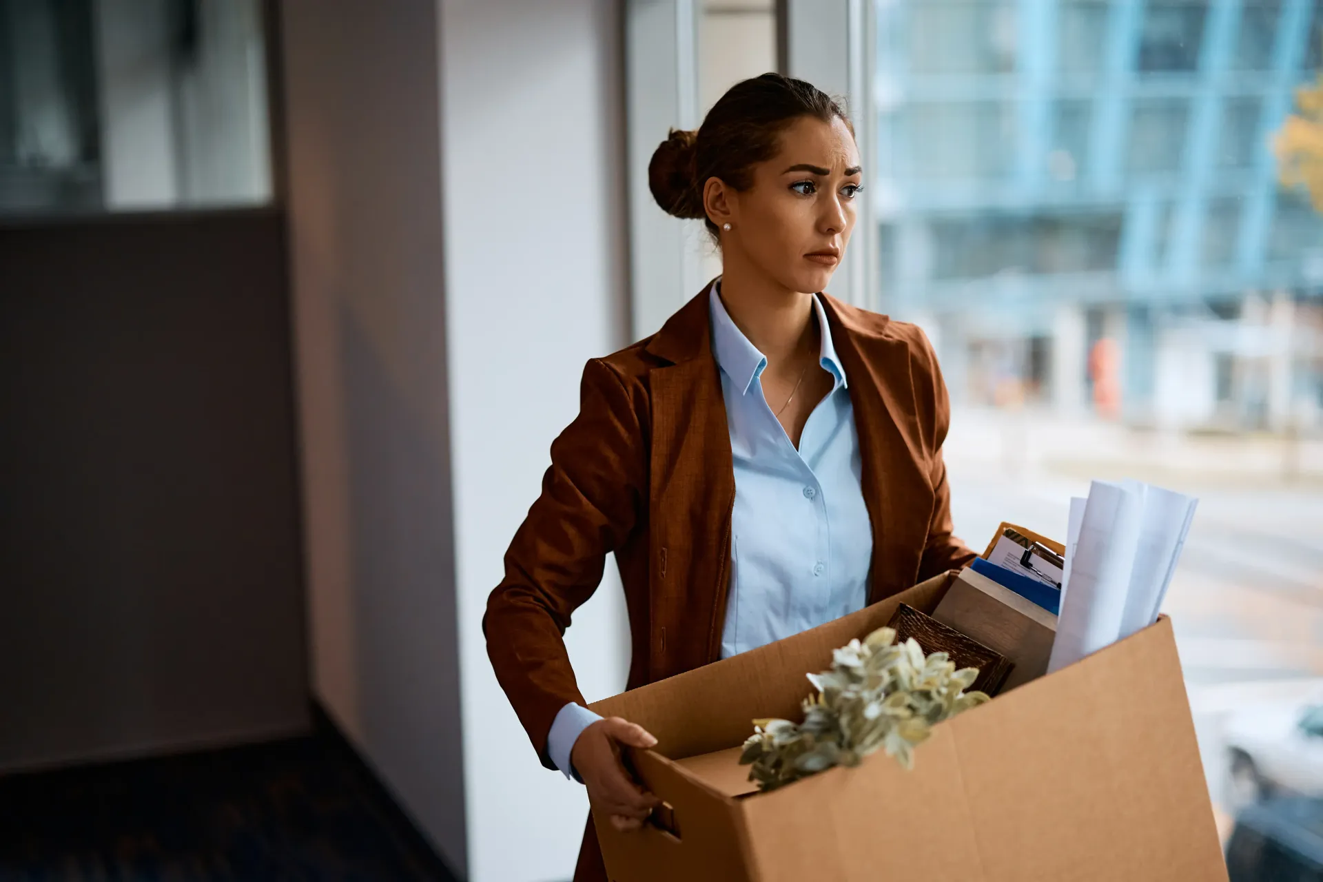 A woman is carrying a box of her belongings out of an office.