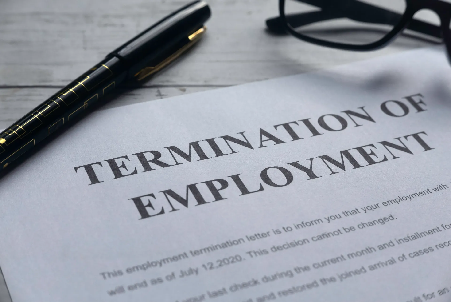 A termination of employment letter atop a desk with a pen and glasses. 