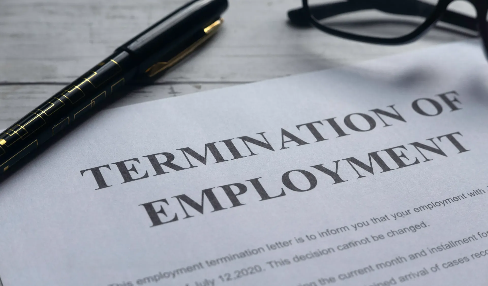 A termination of employment letter atop a desk with a pair of glasses and a pen.