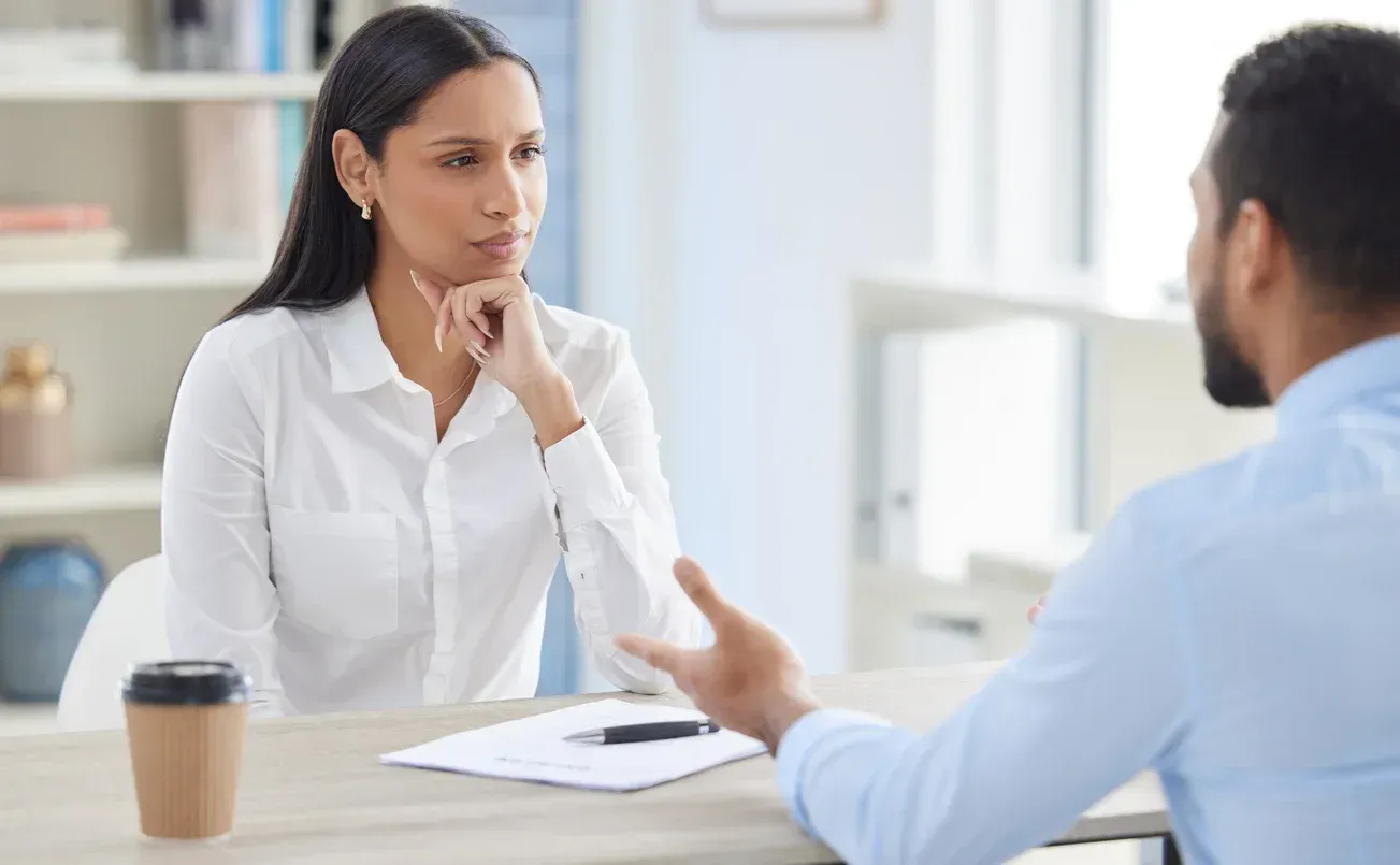 Man and woman sitting across from one another in an office setting, having a work discussion. 