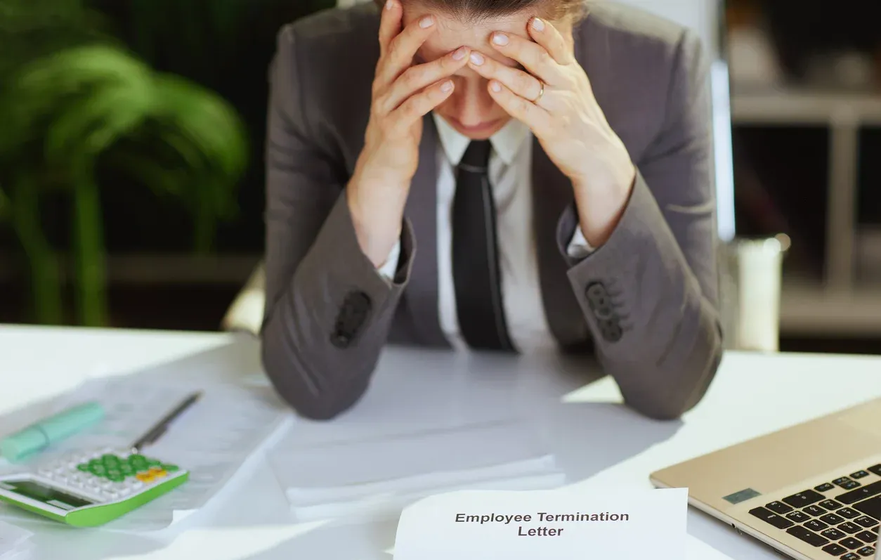 Employee in business suit, hands on head, looking stressed at termination letter on desk.
