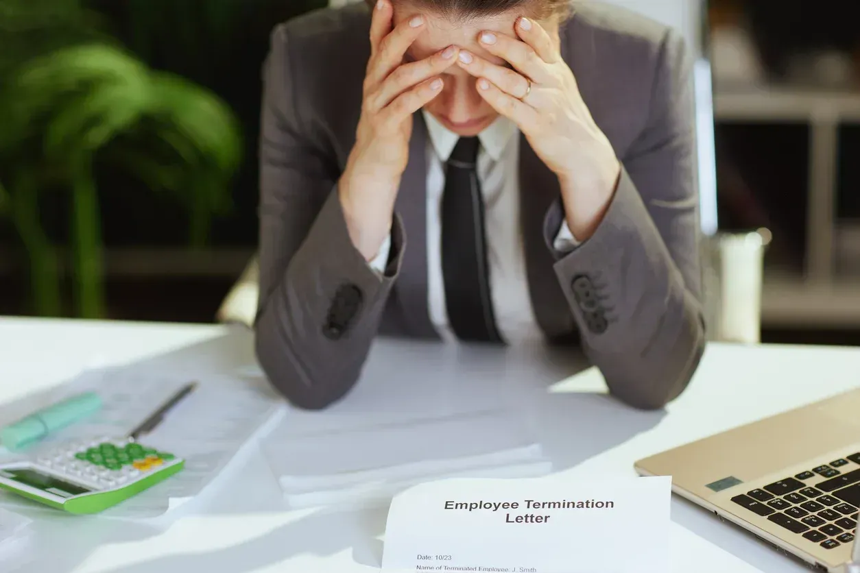Employee in business suit, hands on head, looking stressed at termination letter on desk.
