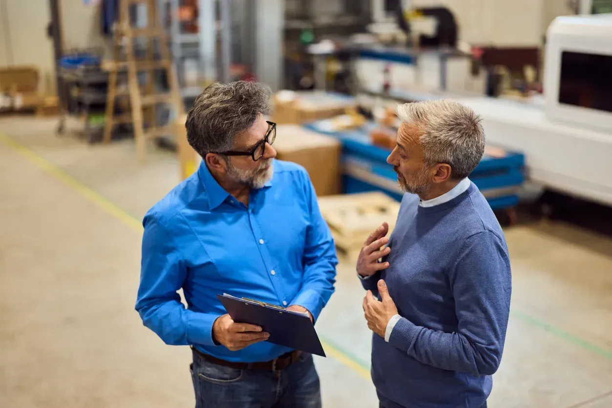 Two men in a factory discussing, one holding a tablet.