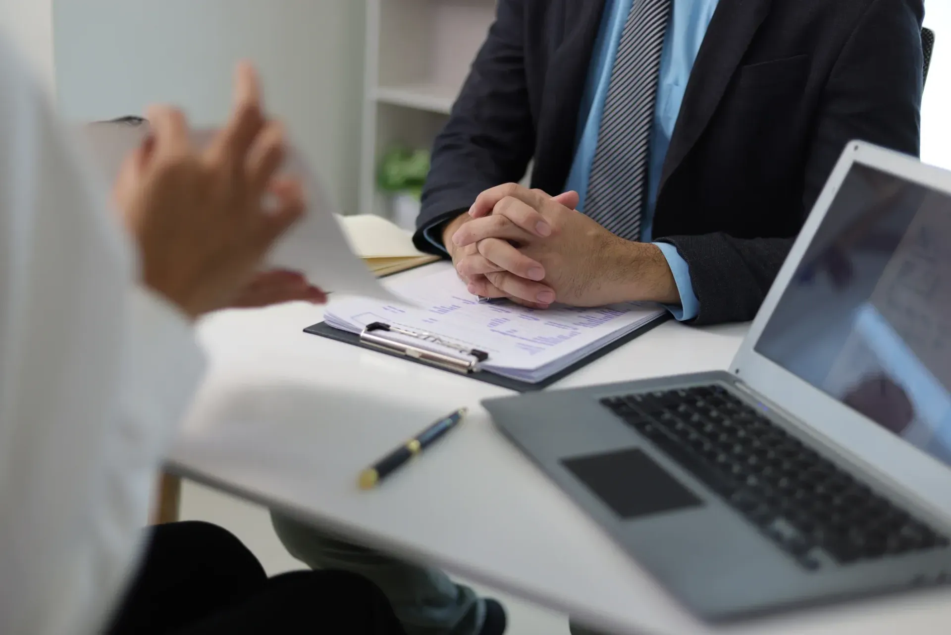 A person in white reports to a man in a suit, sitting at a desk.